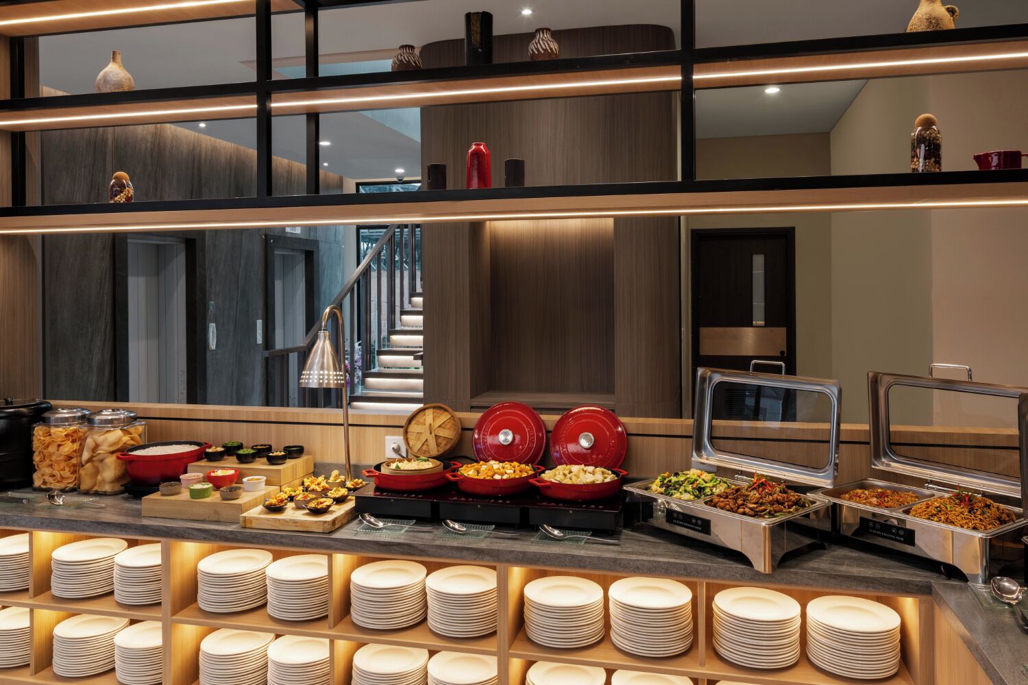 Una mesa de buffet con diversos alimentos, incluyendo fuentes y bandejas, y una pila de platos.