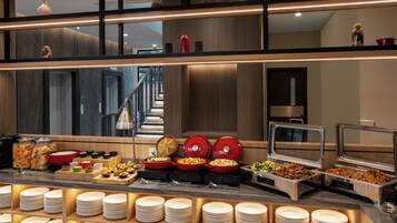 Una mesa de buffet con diversos alimentos, incluyendo fuentes y bandejas, y una pila de platos.