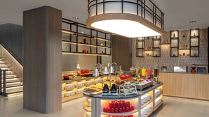 Un hall d’hôtel moderne avec un espace buffet central, un escalier et un comptoir d’accueil.