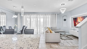 A modern living room with a marble floor, a sofa, a coffee table, and a TV mounted on the wall. - NEW! Solterra Townhome, Private Pool, 4 Bedroom, 3.5 Bathroom, 15 min to Disney (Davenport)