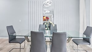 A modern dining area with a glass table and four chairs, a decorative light fixture, and a view into a kitchen area. - NEW! Solterra Townhome, Private Pool, 4 Bedroom, 3.5 Bathroom, 15 min to Disney (Davenport)