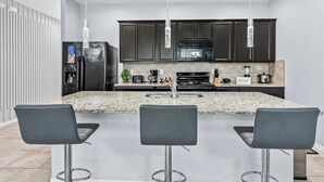 A modern kitchen with dark cabinets, a granite countertop, and three bar stools. - NEW! Solterra Townhome, Private Pool, 4 Bedroom, 3.5 Bathroom, 15 min to Disney (Davenport)