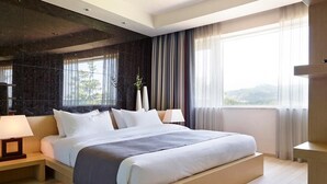 A modern hotel bedroom with a large bed, bedside lamps, a dark accent wall, and a view of the outdoors. - Kinock Pet Hotel (Gyeongju)