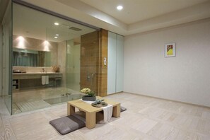 A modern hotel room with a glass partition, a wooden table with cushions, and a view of the bathroom. - Kinock Pet Hotel (Gyeongju)
