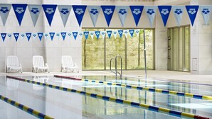 An indoor swimming pool with clear lanes, white lounge chairs, and blue and white flags on the walls. - Kinock Pet Hotel (Gyeongju)