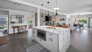 Une cuisine spacieuse dotée d’un îlot en marbre, de luminaires suspendus modernes et d’un grand téléviseur.
