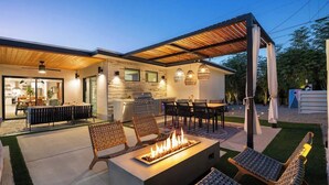 Une terrasse extérieure moderne, dotée d’un foyer, de sièges et d’un espace repas couvert.