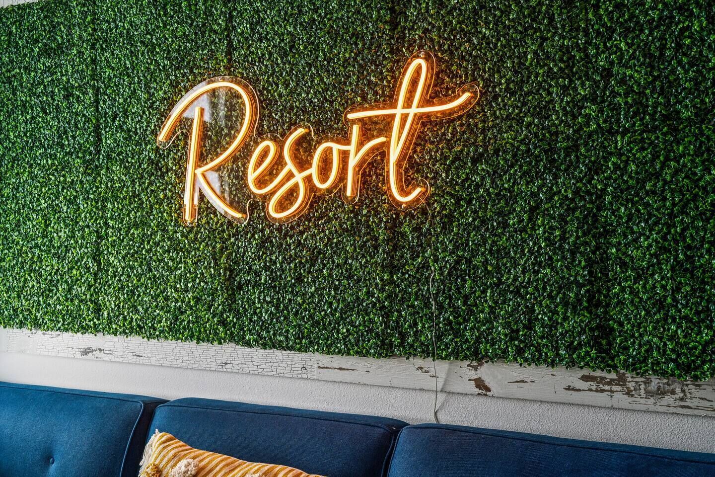 Eine Neonreklame mit der Aufschrift "Resort" an einer grünen, belaubten Wand.