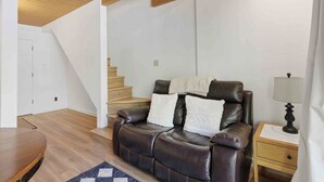Un saló amb un sofà de cuir, una taula baixa de fusta, una làmpada i una escala.