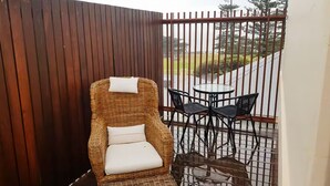 A wicker chair with white cushions, a small round table, and two black chairs, all enclosed by a metal fence. - Penthouse Ozone in Queenscliff (Queenscliffe)