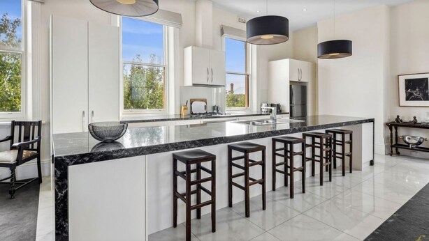 A modern kitchen with a large island, bar stools, and pendant lighting. - Penthouse Ozone in Queenscliff (Queenscliffe)