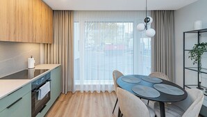 A modern kitchen with a dining area, wooden cabinets, a built-in oven, and a large window with curtains. - Vytauto 43 Residence – Lietūkis by Domvia (Kaunas)