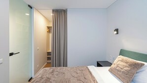 A modern bedroom with a bed, a nightstand, a wall-mounted light, and a bathroom visible through a glass door. - Vytauto 43 Residence – Lietūkis by Domvia (Kaunas)