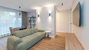 A modern living room with a green sofa, a round coffee table, and a dining area with chairs and a table. - Vytauto 43 Residence – Lietūkis by Domvia (Kaunas)