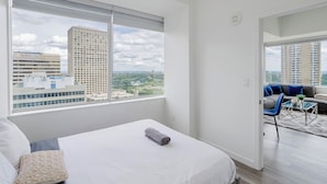 A modern hotel room with a large window, a bed, a sofa, and a small table.