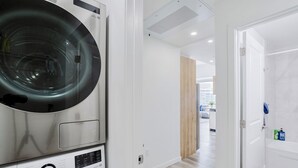 A modern laundry room with a front-loading washing machine and dryer, a wooden floor, and a view of the city through an open door.
