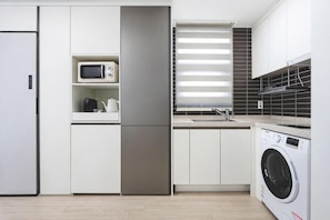 A modern kitchen with a built-in microwave, a washing machine, and a window with blinds. - El Momento Sasang (Busan)