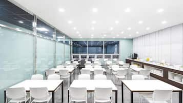 Una sala conferenze con diversi tavoli e sedie, pareti in vetro e un angolo cottura.