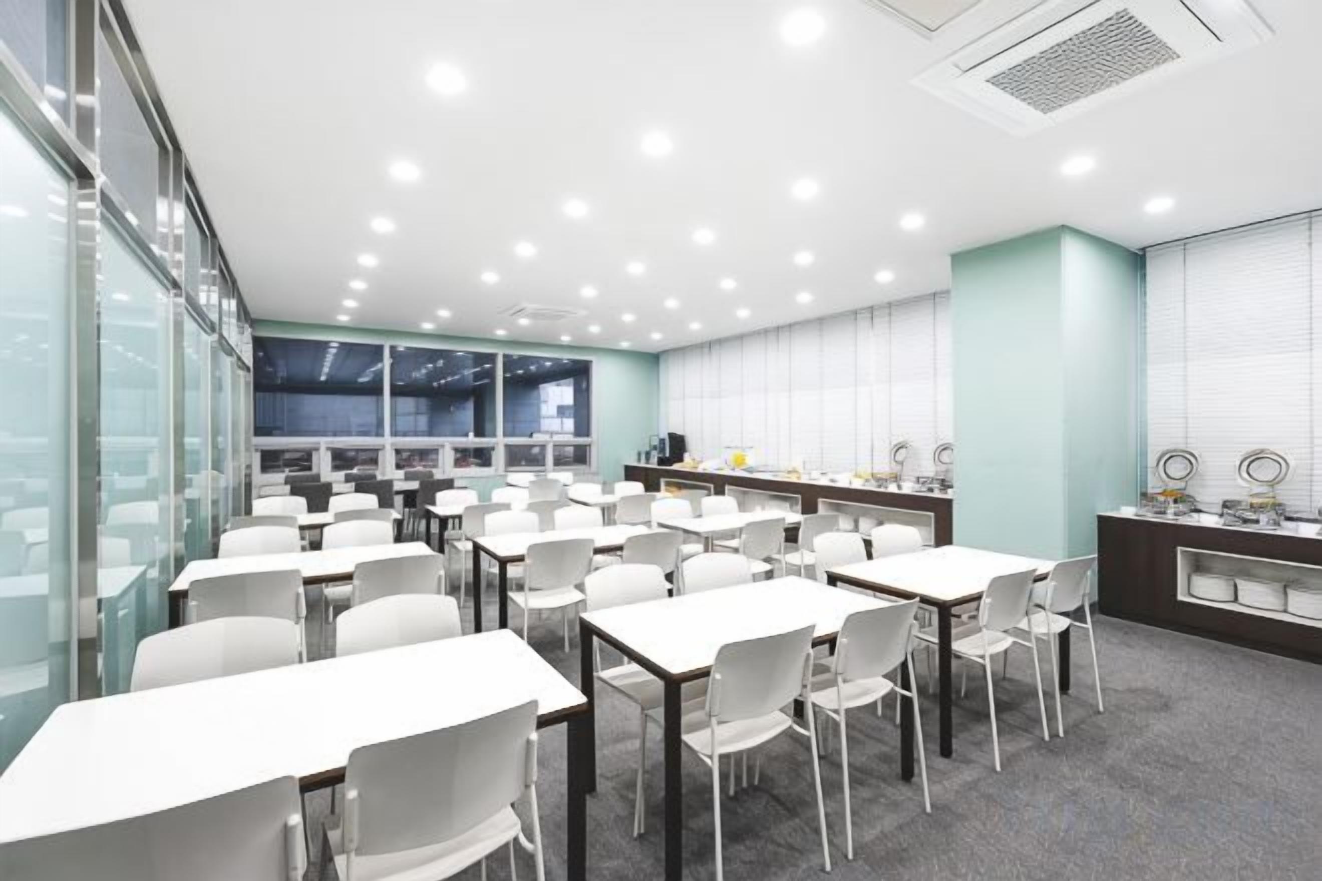 A conference room with tables and chairs, a kitchenette, and a large window.