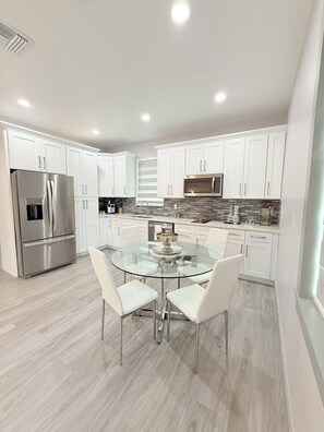 A modern kitchen with white cabinets, stainless steel appliances, and a glass dining table. - Charming 1-bedroom building in fabulous Tampa with AC (Tampa)
