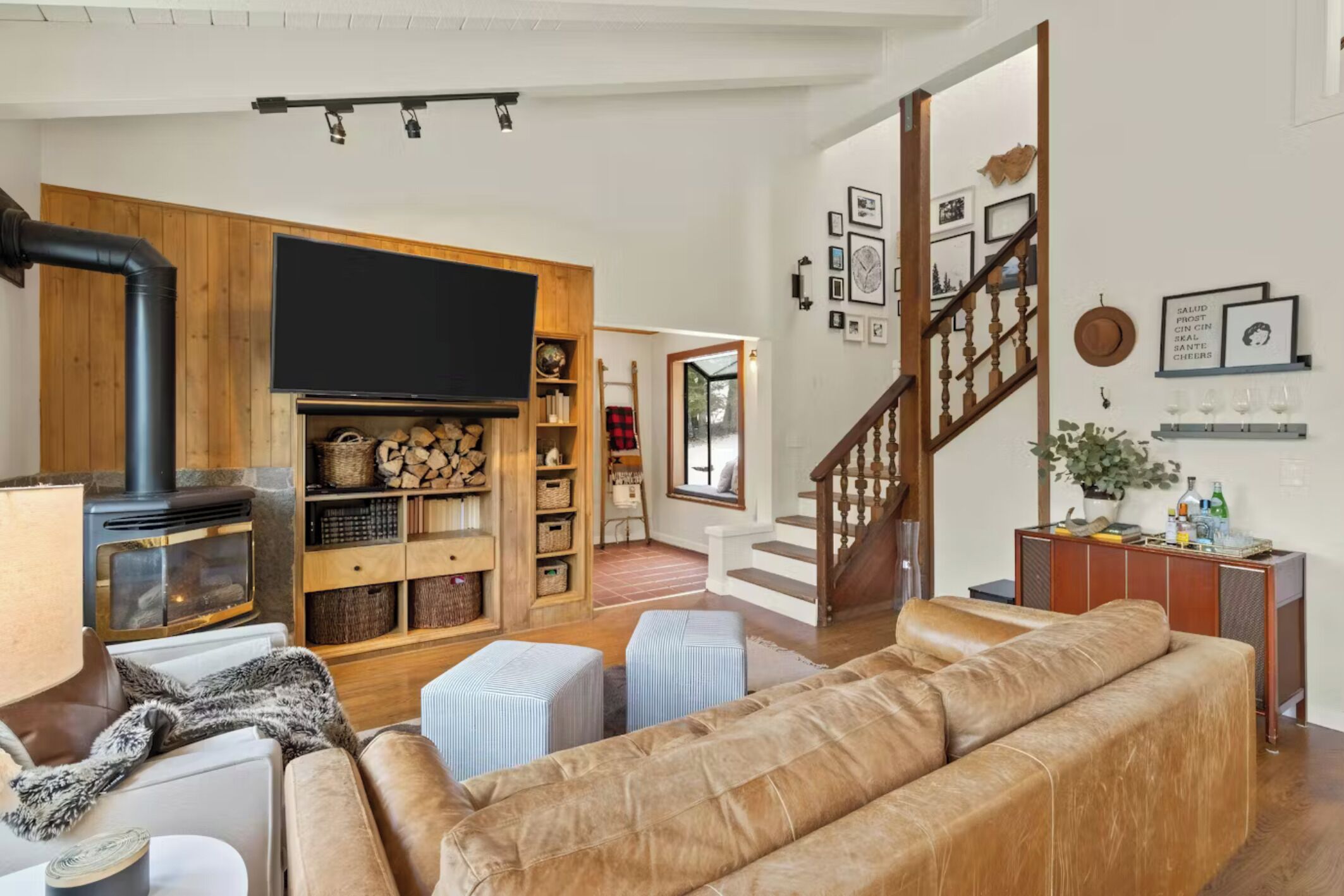 A cozy living room with a fireplace, a sofa, ottomans, and a TV.