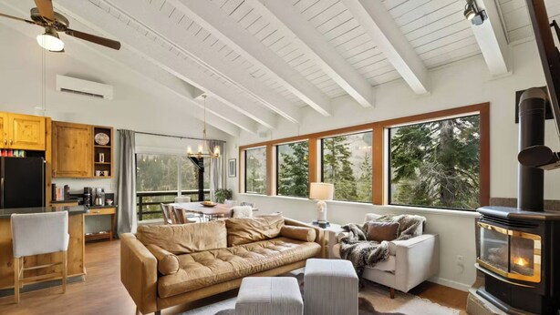 A spacious living area with a large window, a fireplace, and a cozy seating arrangement. - Panoramic Peaks at Alpine by Tahoe Getaways - Pet-Friendly, A/C, Hot Tub, Shuttle & Stunning Views (Alpine Meadows)