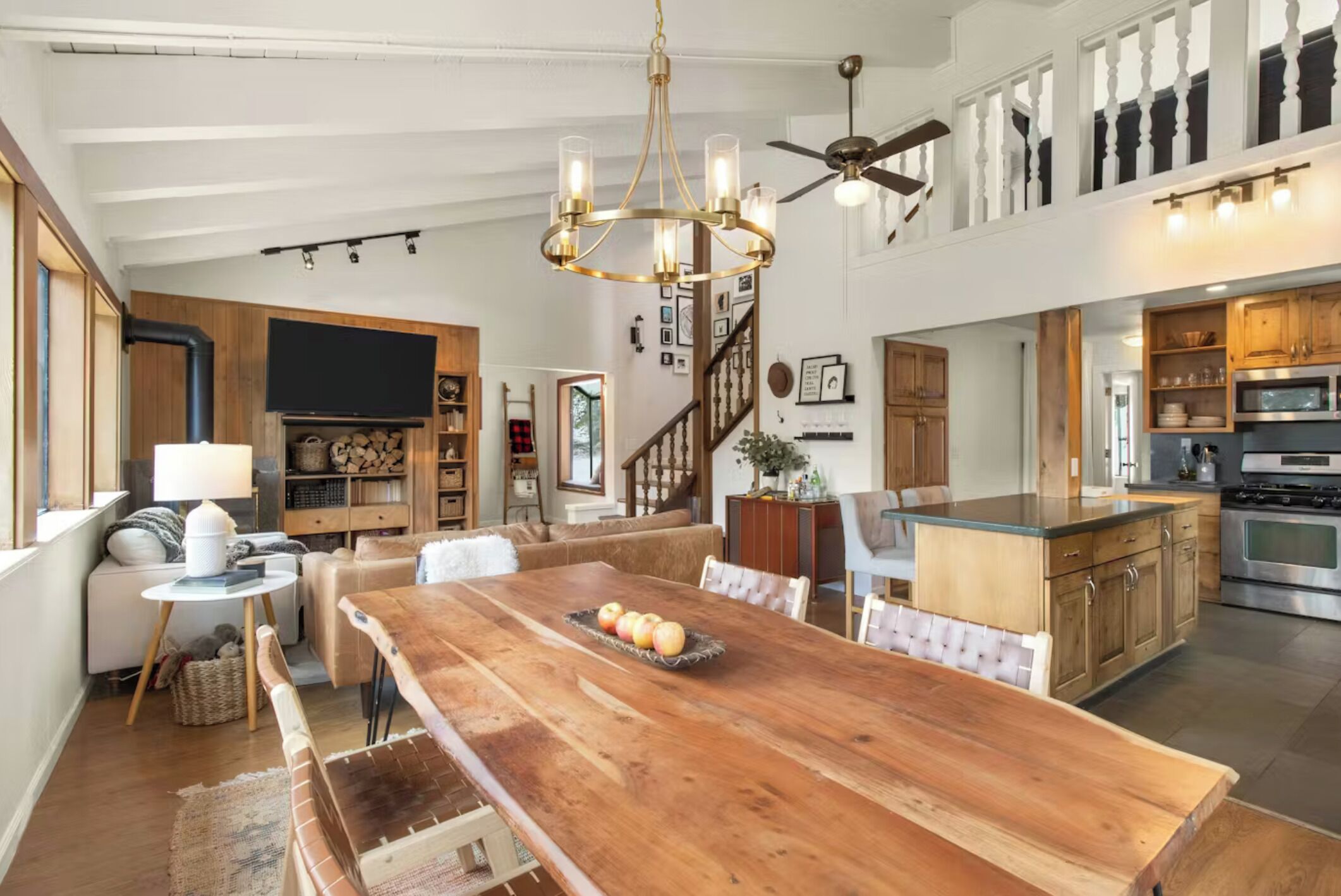 A spacious living area with a large wooden dining table, a chandelier, and a ceiling fan.