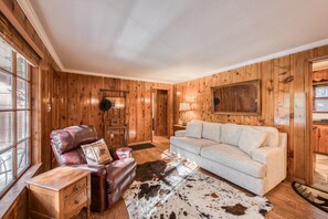 A room with wooden paneling, a leather armchair, a light-colored sofa, a cowhide rug, and a wooden cabinet. - Diana's Cabin by Tahoe Getaways - Pet-Friendly 2BR in Kings Beach w/ Backyard + Walk to Lake! (Tahoe Vista)