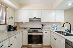A modern kitchen with white cabinets, stainless steel appliances, and a built-in oven. - Sun Stack at Runaway Bay 251 (Bradenton Beach)