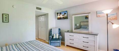 Un dormitorio con cama, una silla, cómoda, ventilador de techo y decoración en la pared.