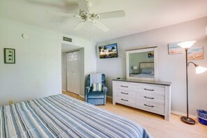 A bedroom with a bed, a chair, a dresser, a ceiling fan, and wall art. - Sun Stack at Runaway Bay 251 (Bradenton Beach)
