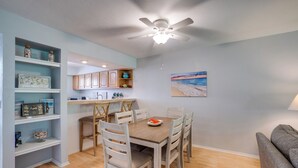 Un comedor con una mesa y sillas de madera, un ventilador de techo y una estantería decorada.