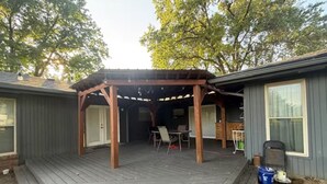 Ein überdachter Patio-Bereich mit Holzterrasse, einer Pergola und einem Tisch mit Stühlen.