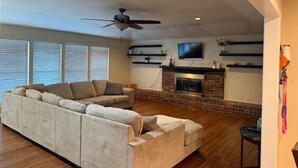 Ein Wohnzimmer mit Ecksofa, Kamin, Deckenventilator und an der Wand montiertem Fernseher.