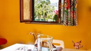 A dining area with a table set for two, a window with colorful curtains, and a view of greenery outside. - Casa Nicanto (Meta)