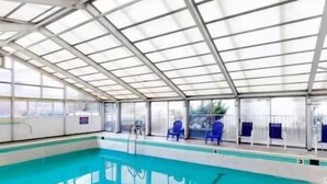 Ein überdachter Indoor-Pool mit großen Glaswänden, blauen Liegestühlen und einer Metallkonstruktion.