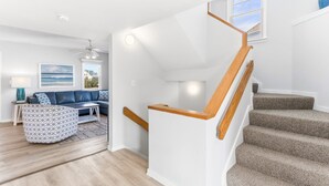 A modern living room with a wooden staircase, a blue sofa, and a view of the outdoors.