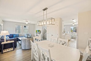 A modern living room with a sofa, a coffee table, and a dining area with a table and chairs. - Pollock: Bright Buxton Townhouse w/ Ocean Views (Buxton)