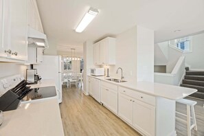 A modern kitchen with white cabinetry, a built-in microwave, and a stainless steel sink. - Pollock: Bright Buxton Townhouse w/ Ocean Views (Buxton)