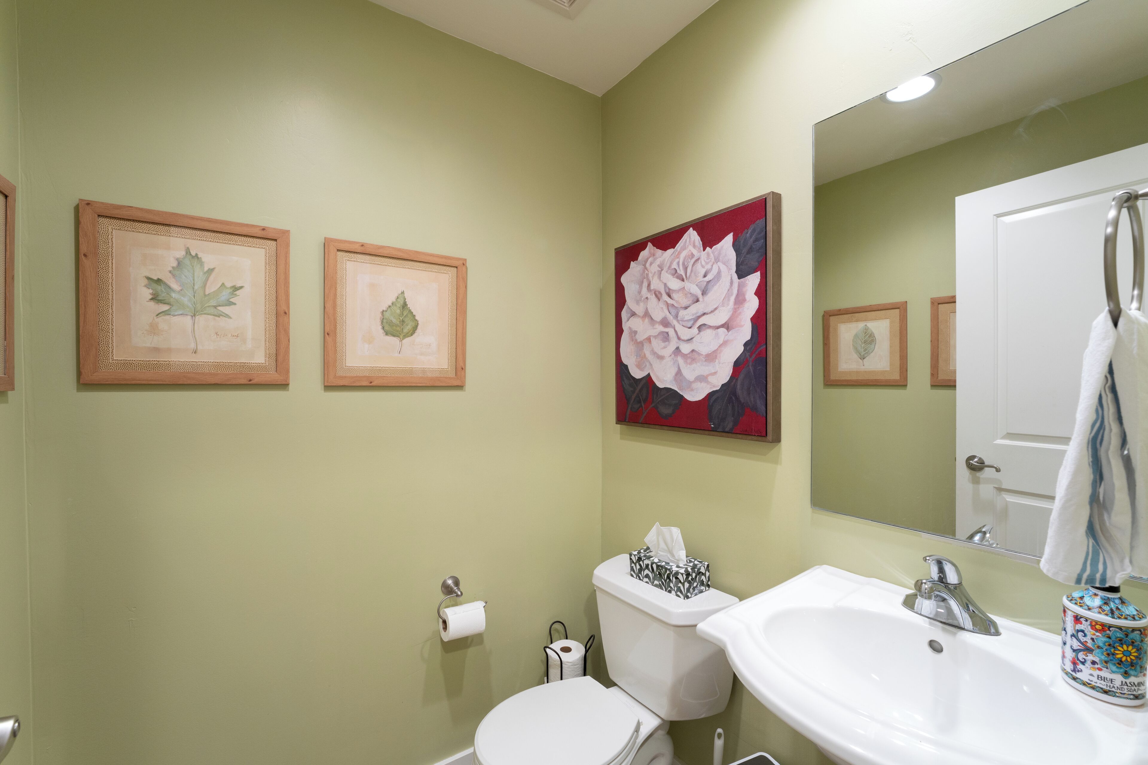 Un baño con inodoro, lavamanos y una obra de arte enmarcada en la pared.