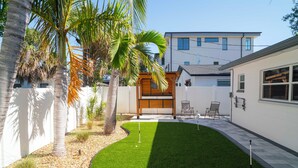 Une maison moderne dotée d’une pelouse bien entretenue, de palmiers et d’un espace patio aménagé avec des chaises.