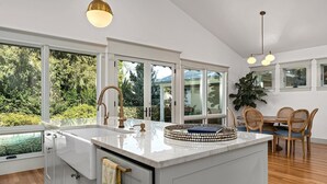 Una cocina moderna con una isla grande, armarios blancos y vistas al exterior.
