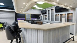 Eine moderne Bar mit einer Theke, Hockstühlen und einem an der Wand befestigten Fernseher.