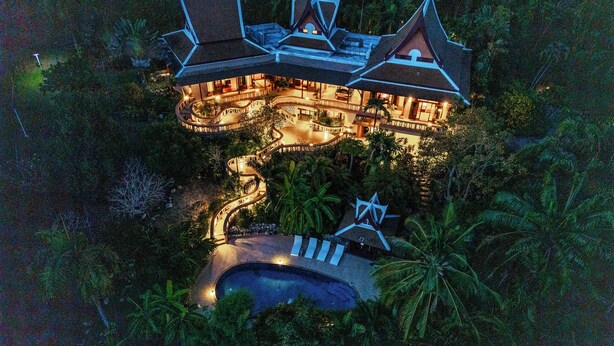 An aerial view of a resort with a large swimming pool, multiple guest rooms, and a well-lit outdoor area surrounded by tropical vegetation. - 7BR Luxury Pool Villa - Layan Beach (Tambon Choeng Thale)