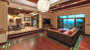 A spacious living area with a large sofa, a dining table with chairs, a television, and a view of the outdoors through large windows. - 7BR Luxury Pool Villa - Layan Beach (Tambon Choeng Thale)