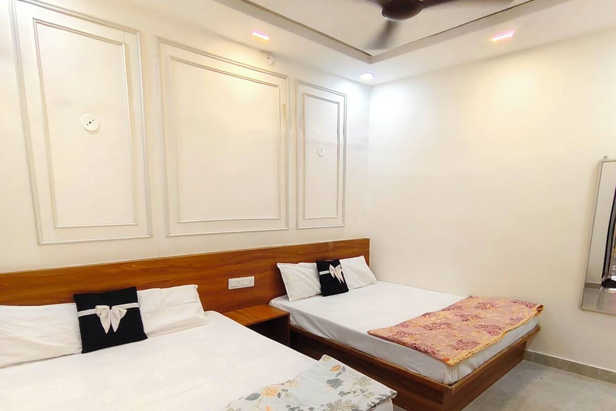 Une chambre d’hôtel avec deux lits, des têtes de lit en bois, des murs blancs et un ventilateur de plafond.