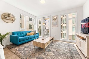 A modern living room with a blue sofa, a coffee table, and a TV on a cabinet. - The K-Town 2BD Haven - Hot Tub, Gym & Parking (Los Angeles)