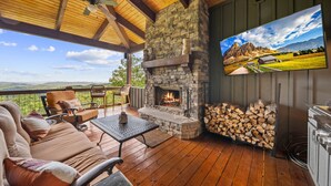 A cozy outdoor patio with a stone fireplace, comfortable seating, and a TV mounted on the wall. - Resort Home–Scenic Views-Whispering Ridge Estate (Boone)