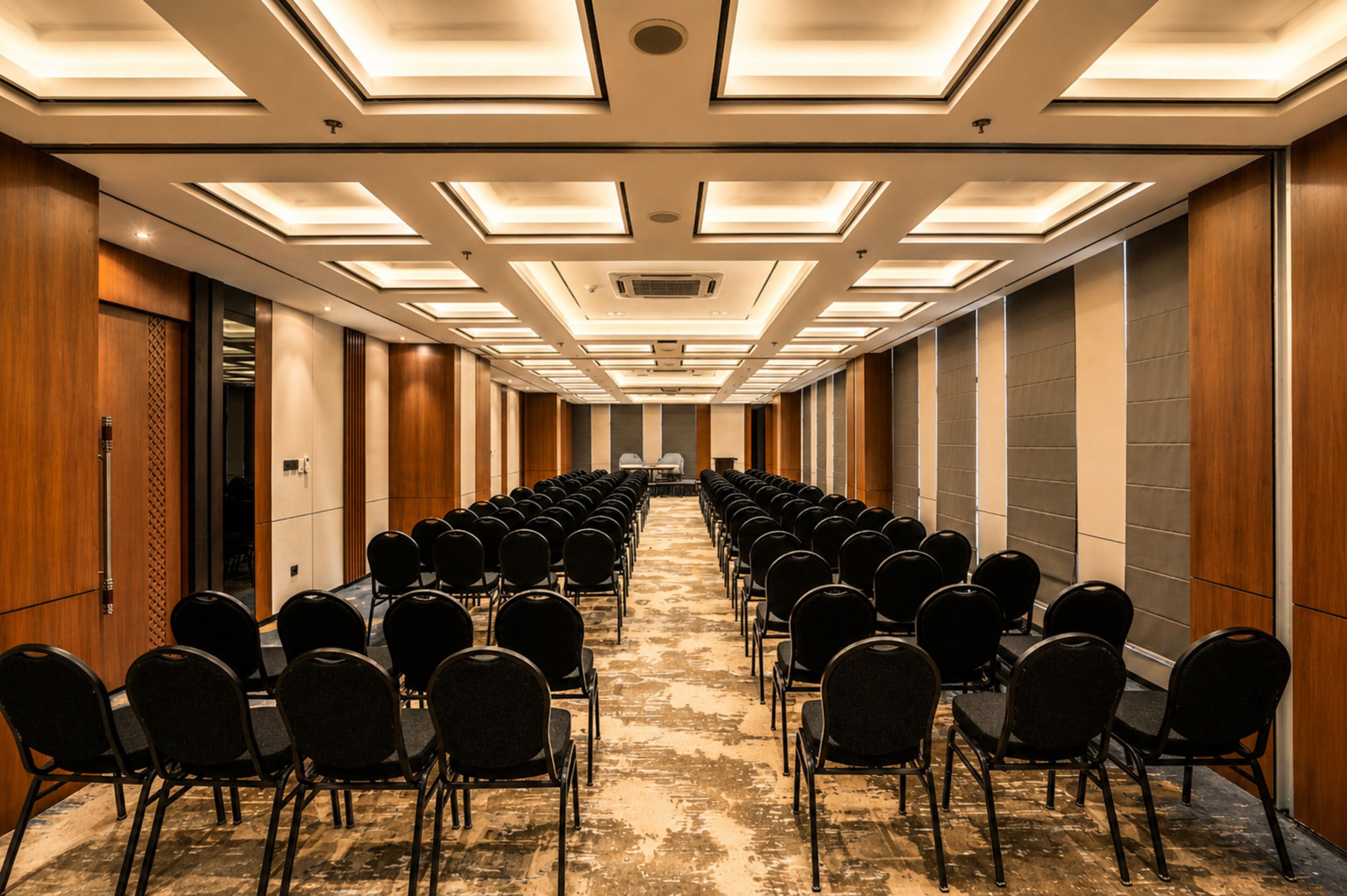 A conference room with rows of chairs, a long table, and a ceiling with recessed lighting.