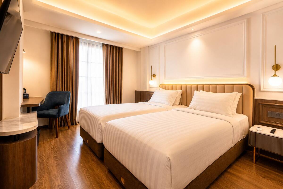 Quarto de hotel com duas camas, uma escrivaninha, uma cadeira e uma televisão.